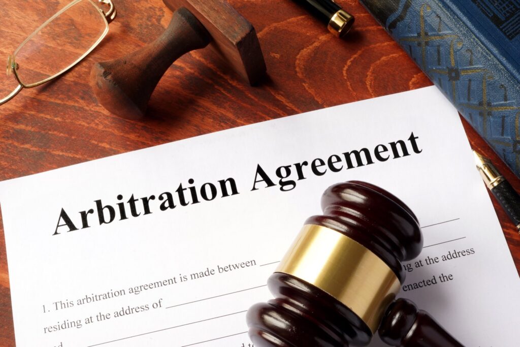 Paper that says Arbitration Agreement with a gavel on top next to glasses