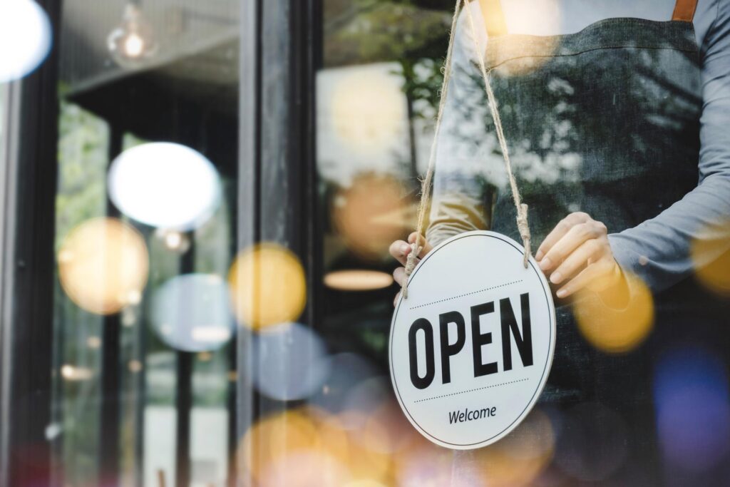 A person in an apron behind glass in a storefront flips an open sign around.