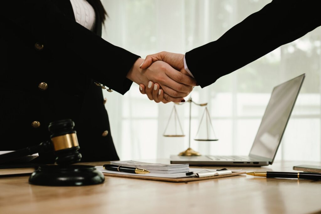 Two hands shaking hands across a table with a gavel and paperwork on it