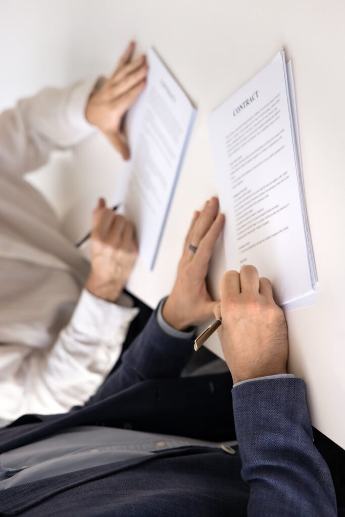 Zoomed in picture of two people sitting at a desk signing contracts