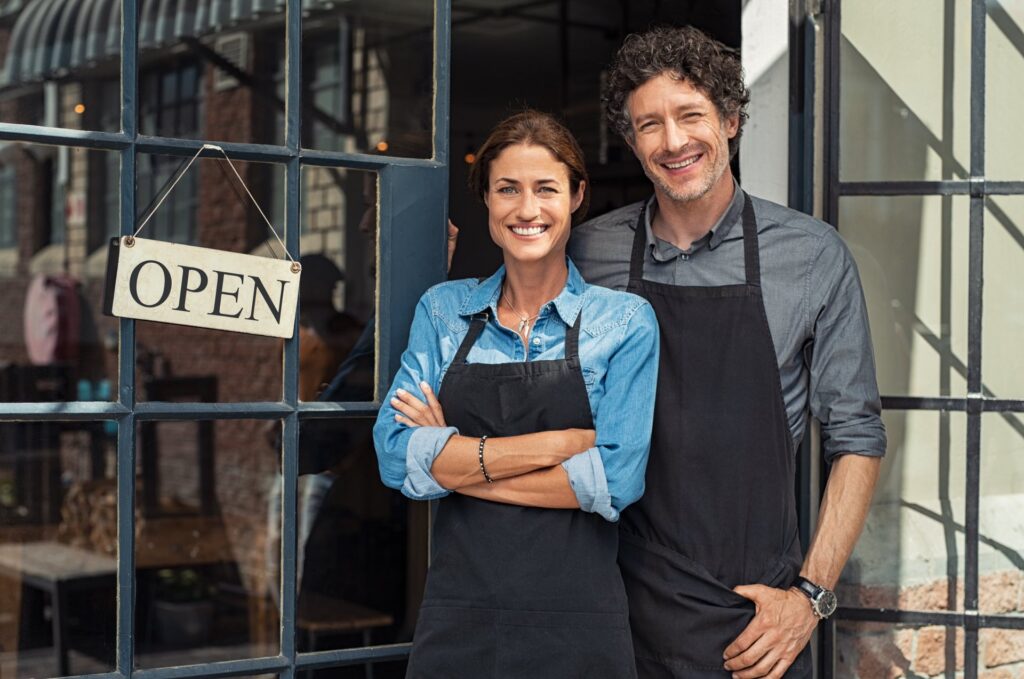 Two people standing in front of a window with a sign that says open