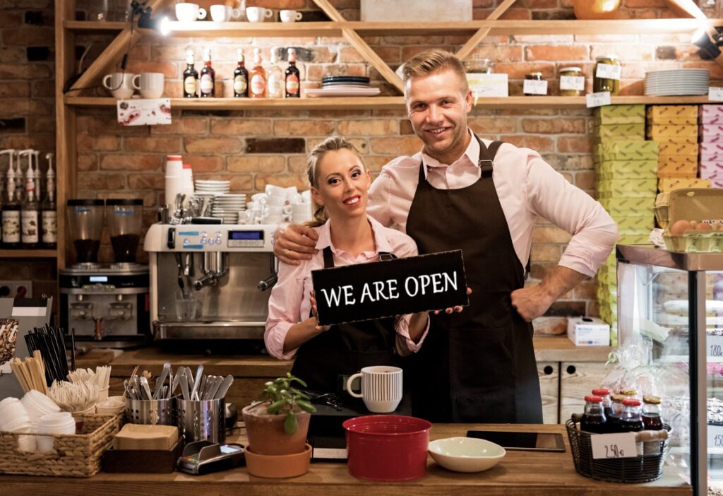 Two people holding up a sign that says we are open